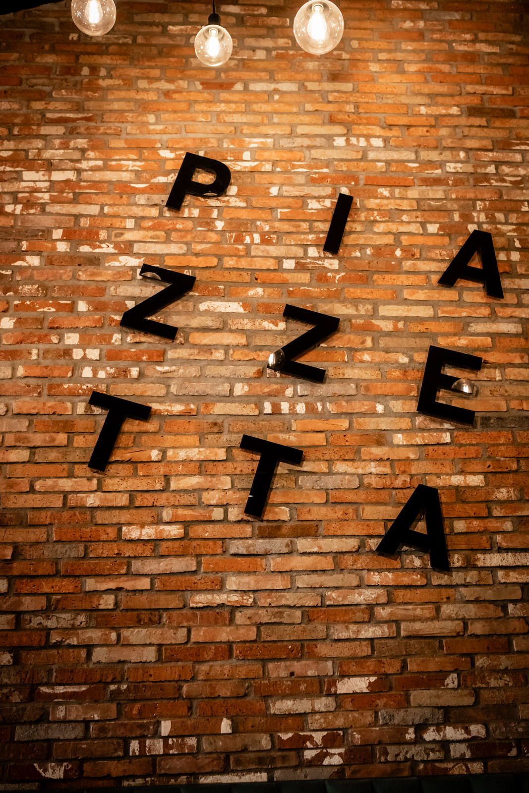 Enseigne Piazzetta en lettres découpées sur un mur de brique