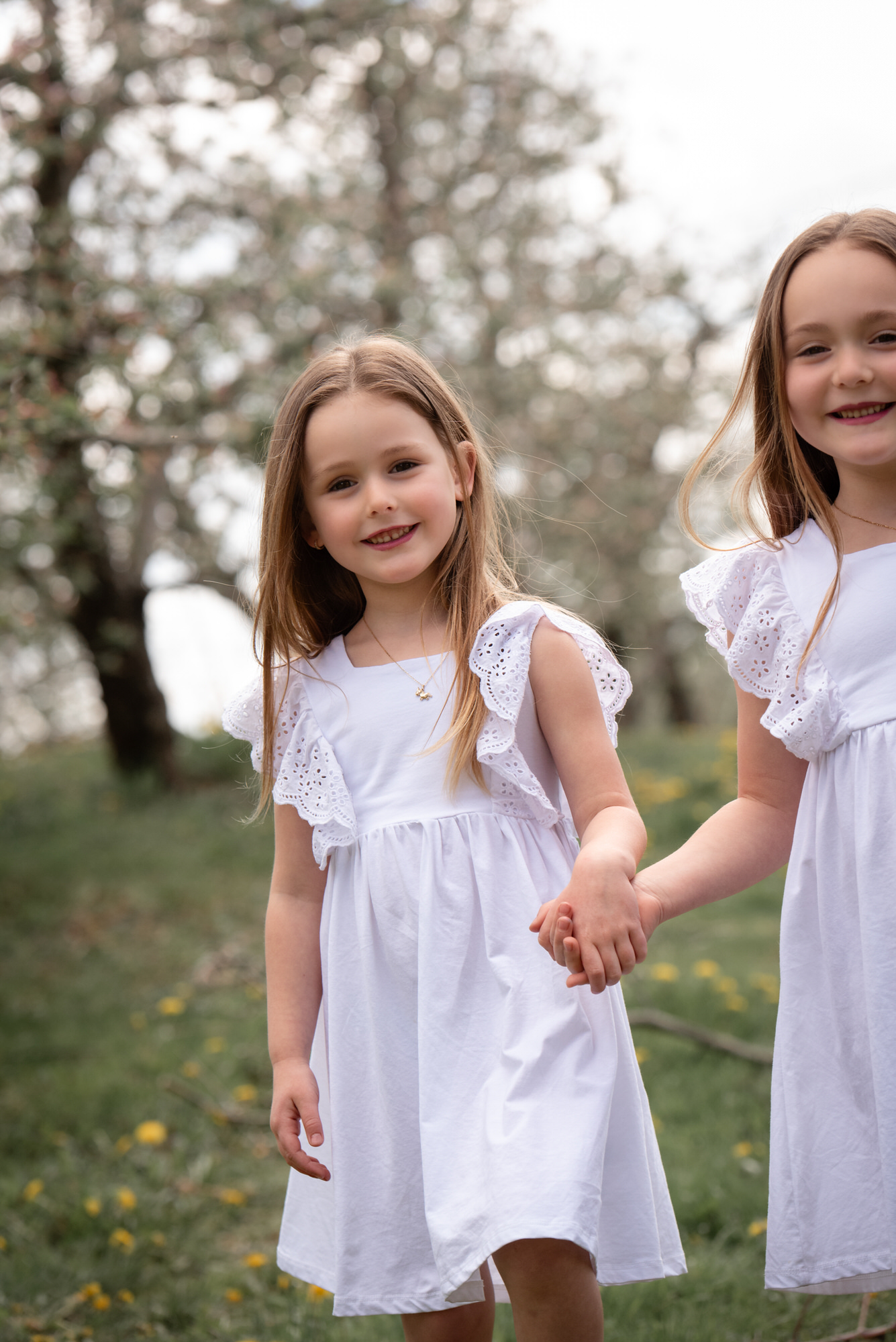 Photo de deux jeunes soeurs qui se tiennent par la main à l'extérieur en robe blanche