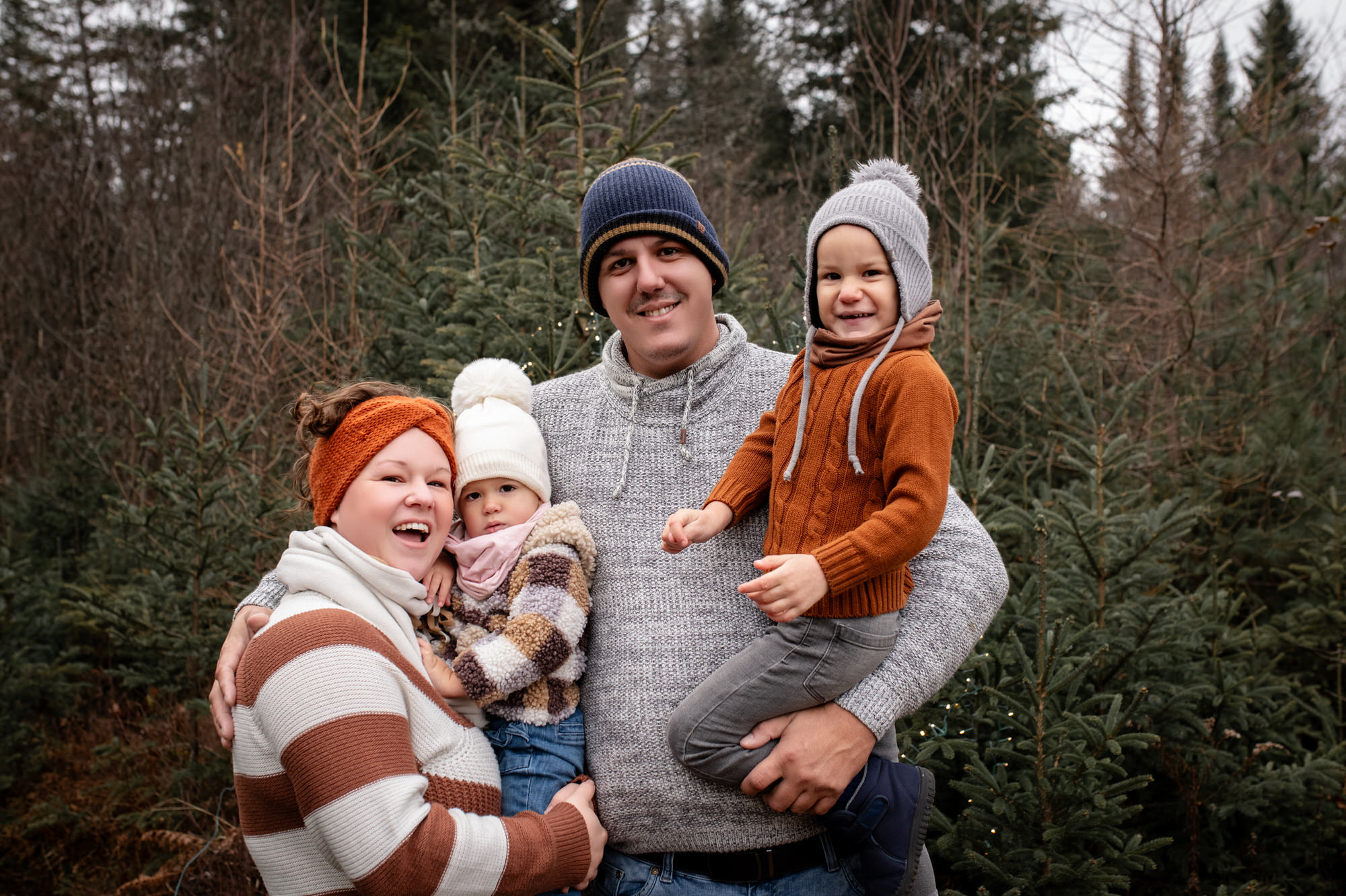 Photo de famille parents et deux enfants dans la nature avec des sapins