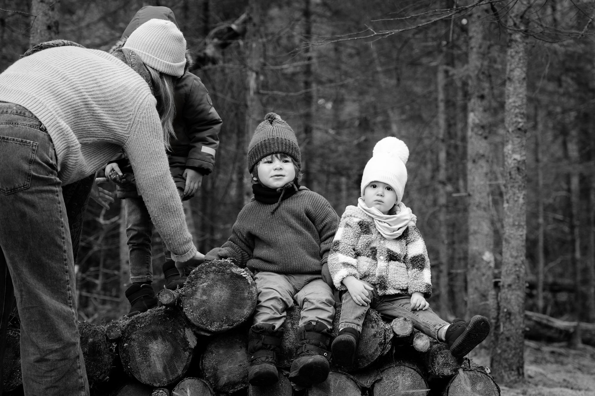 Photo en noir et blanc de trois jeunes enfants assis sur des buches avec tuques